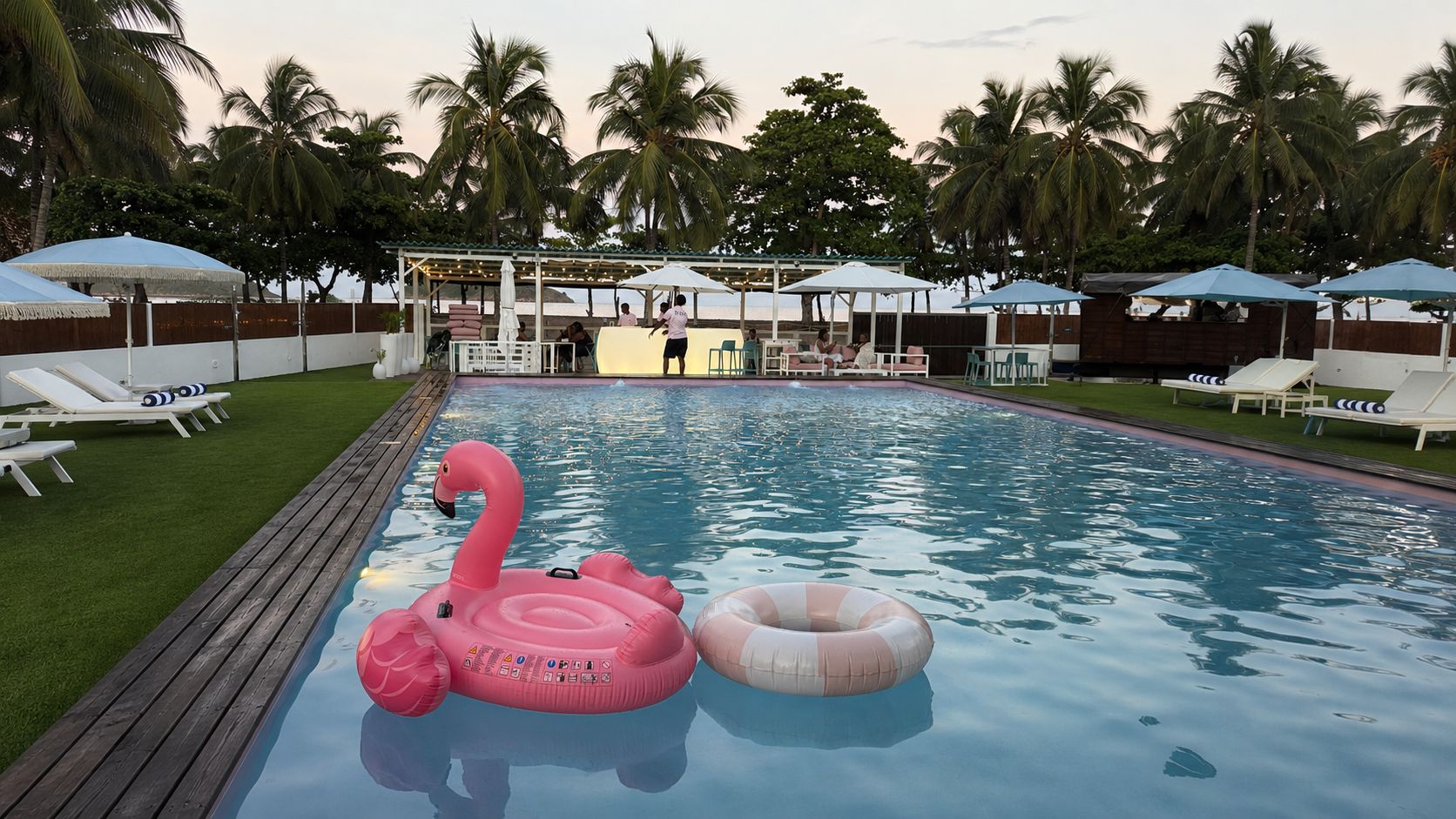Une piscine entourée de palmiers, avec des chaises longues et des parasols.