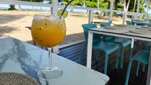 Et glas appelsindrik med et limekvarter og sugerør på et bord med udsigt til en strand og palmer.