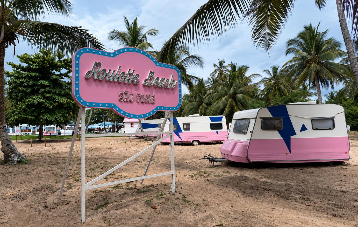 Een bordje voor 'Aoulette Beach' met palmbomen en campers op de achtergrond.