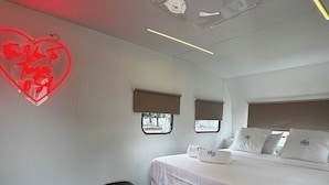 Et hotelværelse med en seng, en sengegavl, et vindue med udsigt, en aircondition og en neon hjertepynt.