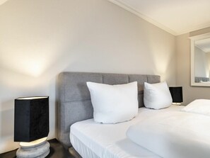 A hotel room with a large bed, two bedside tables, and a nightstand with a lamp. - Holiday Home With 1 Bedroom (Sylt)