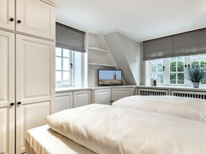 A bedroom with a large bed, a television on a stand, and a window with a view of a lighthouse. - Holiday Home With 1 Bedroom (Sylt)