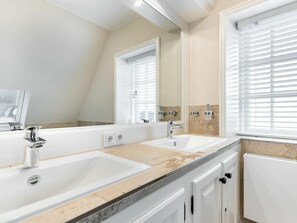 A modern bathroom with two sinks, a large mirror, and a window with blinds. - Holiday Home With 1 Bedroom (Sylt)