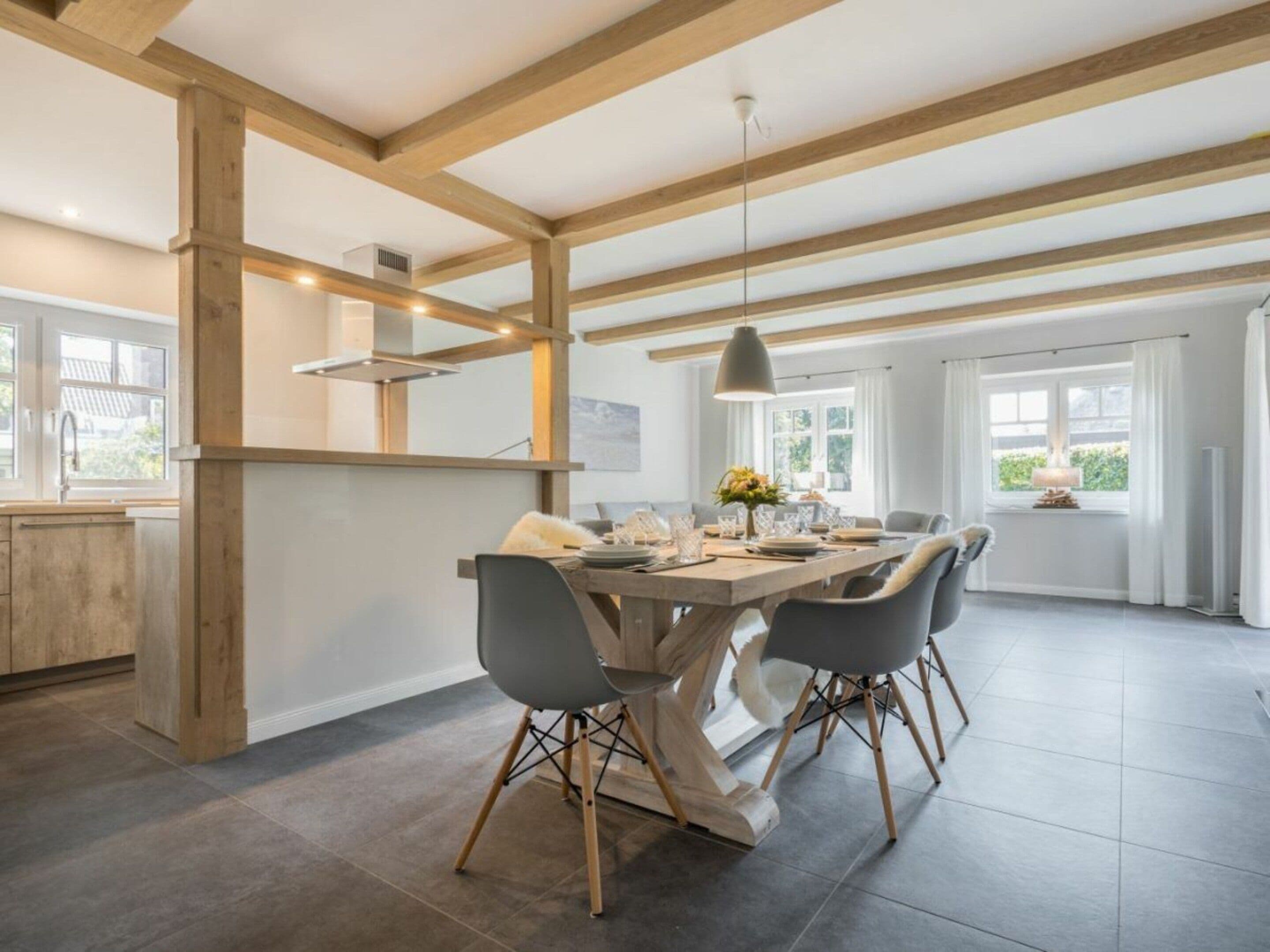 Une cuisine moderne avec des poutres en bois, un coin repas doté d’une grande table et une vue sur l’extérieur.