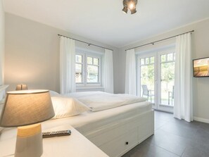 A bedroom with a bed, a bedside lamp, a TV mounted on the wall, and a window with curtains. - "vorn Binnendiek" (St. Peter-Ording)