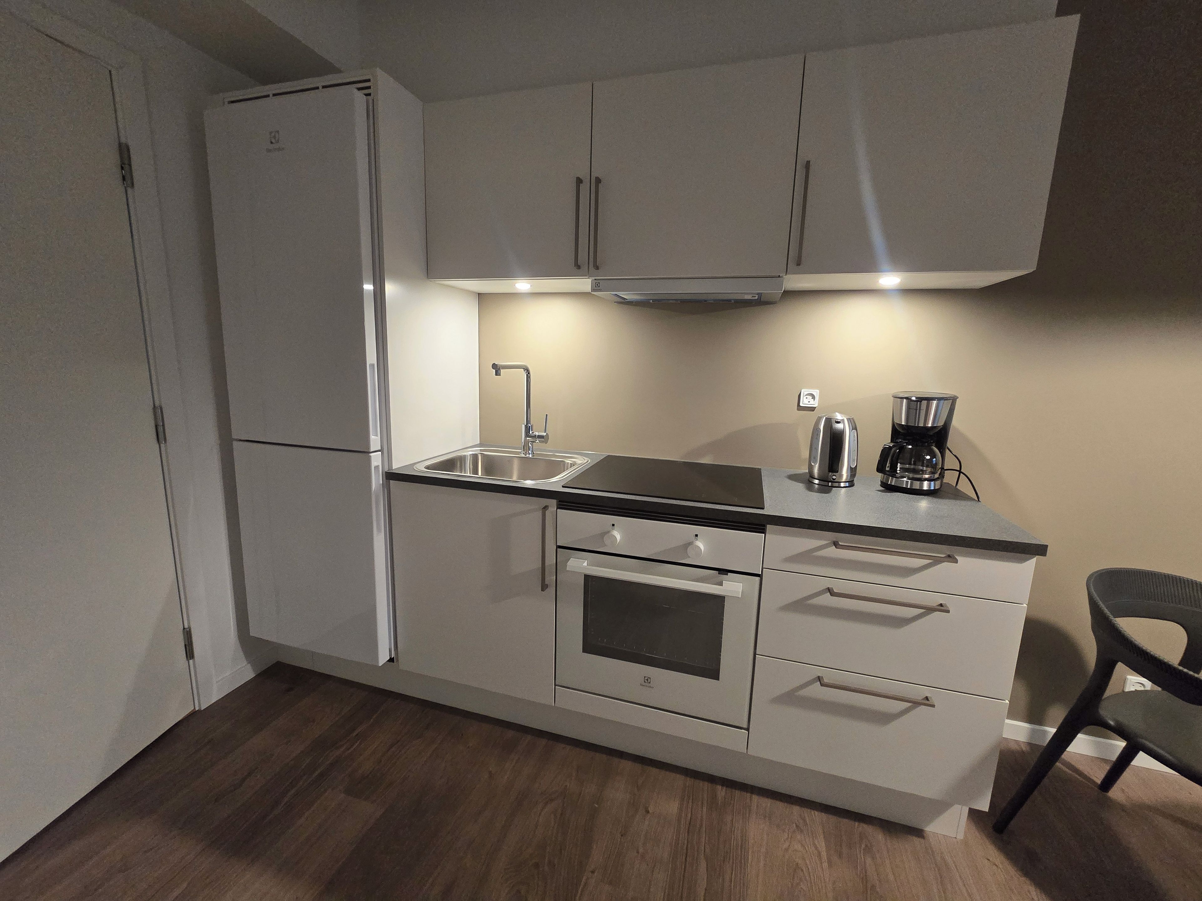 Una cocina compacta equipada con refrigerador, estufa, lavamanos y cafetera.