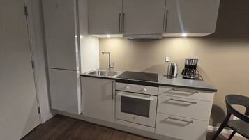Una cocina compacta equipada con refrigerador, estufa, lavamanos y cafetera.