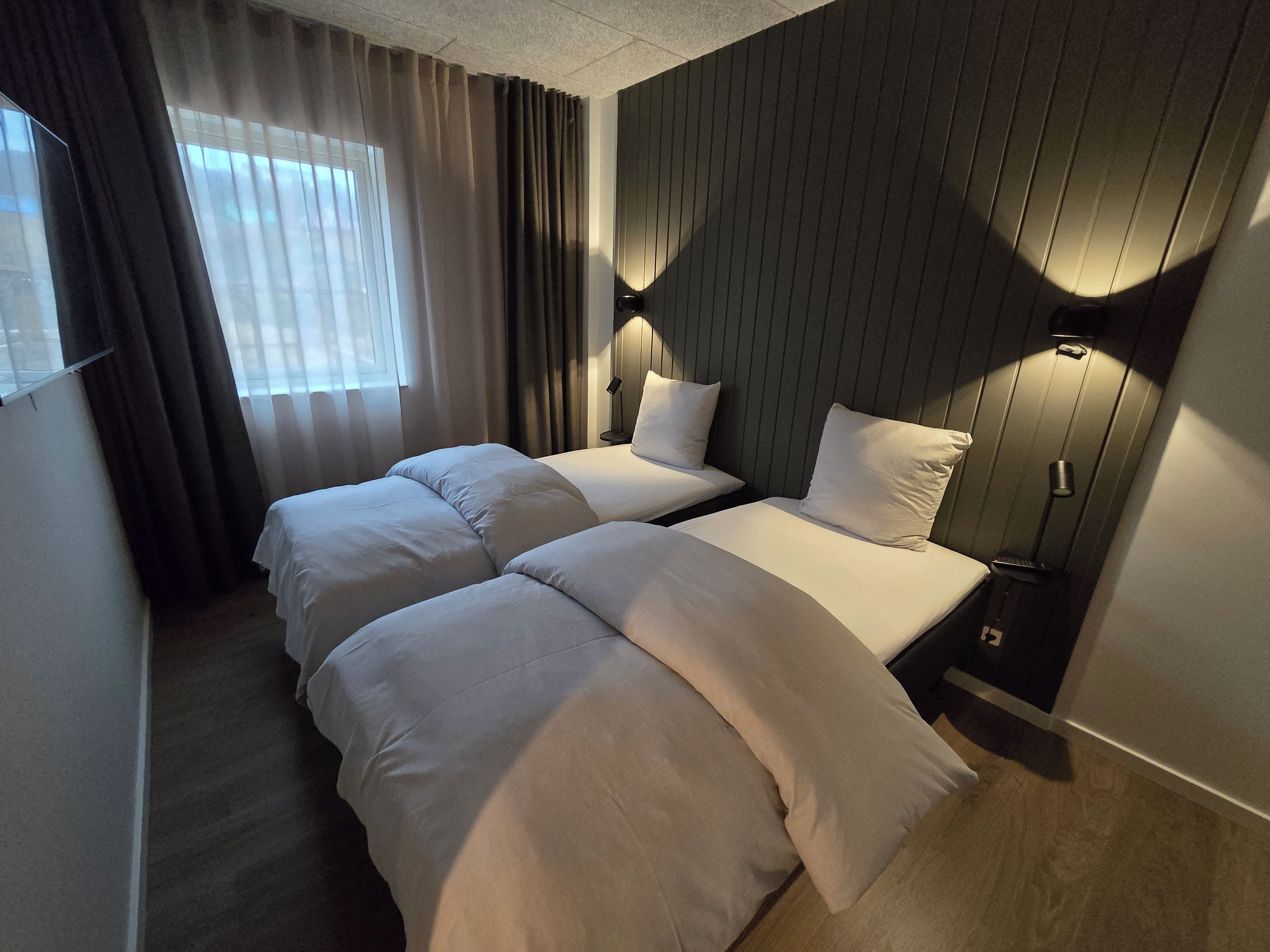 Ein Hotelzimmer mit zwei Betten, einem Fenster mit Vorhängen und einer Wandlampe.