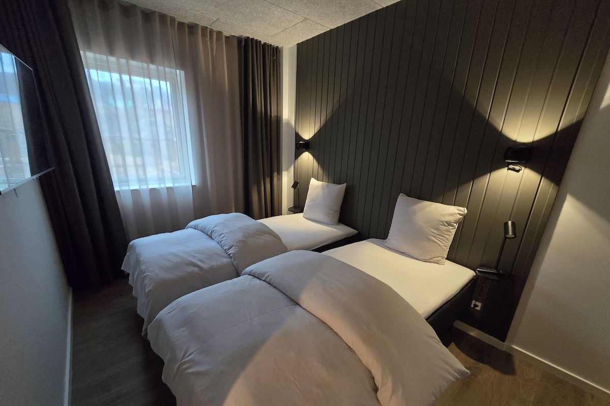 Ein Hotelzimmer mit zwei Betten, einem Fenster mit Vorhängen und einer Wandlampe.