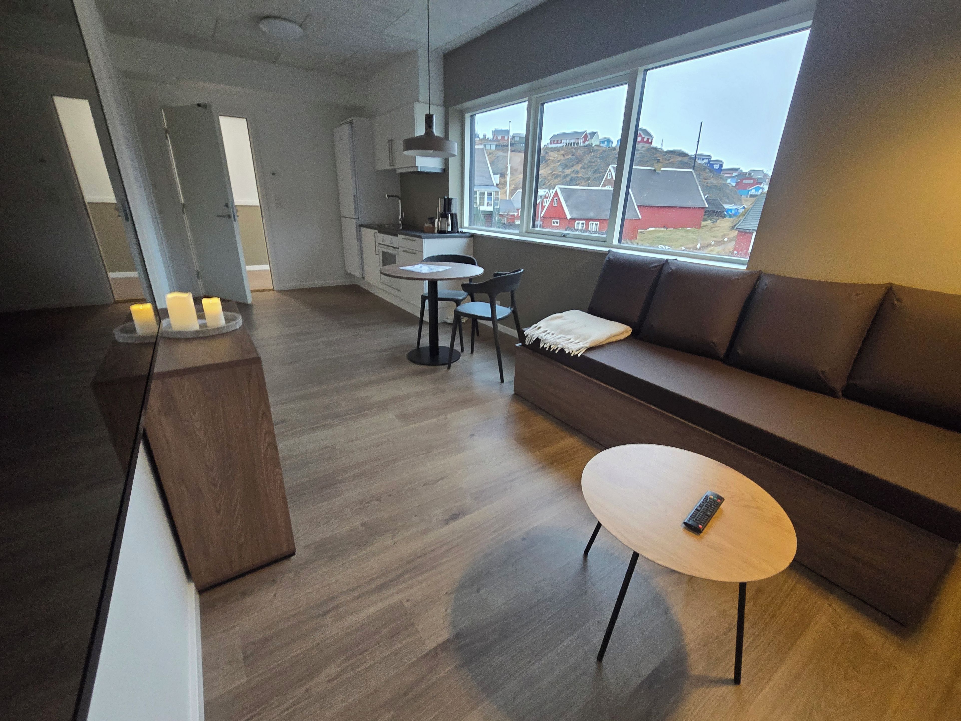 Un salon moderne avec un canapé, une table ronde et un coin cuisine donnant sur une fenêtre.