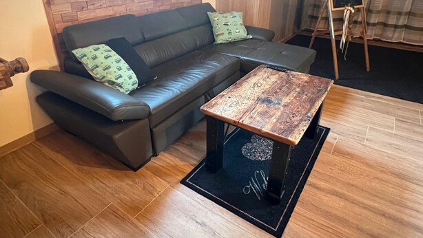 Een moderne woonkamer met een hoekbank, een houten salontafel en een klein schilderstandaard met een schoolbord.