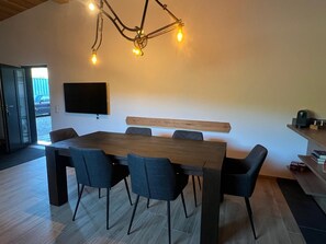 Et moderne spiseområde med et stort træbord, seks stole og et vægmonteret fjernsyn.