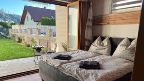 Een slaapkamer met een groot bed, een schuifdeur naar een terras en uitzicht op een huis en tuin.