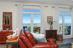 A spacious living room with a leather sofa, a wooden coffee table, and a view of the ocean through large windows. - 🏖️Beachfront with Gulf Views | Multiple Decks | Outdoor Shower | Summer Salt🏖️ (Cape San Blas)