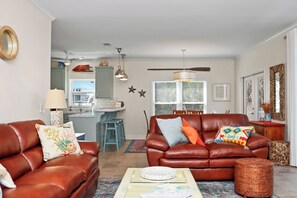 A living room with a brown leather sofa, a coffee table, and a dining area with a kitchen in the background. - 🏖️Beachfront with Gulf Views | Multiple Decks | Outdoor Shower | Summer Salt🏖️ (Cape San Blas)