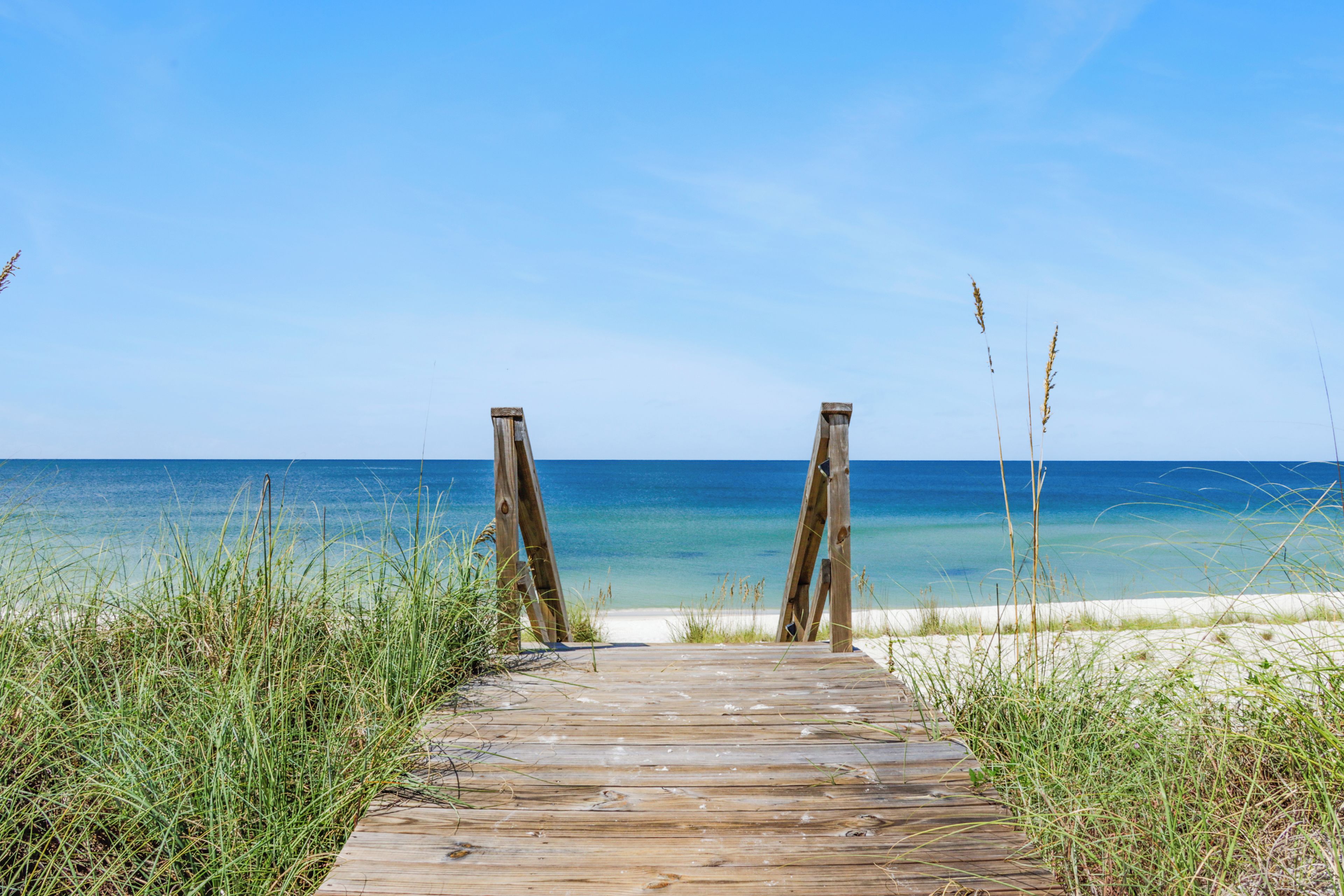 Een houten looppad dat naar een strand leidt met helderblauw water en een zandstrand.