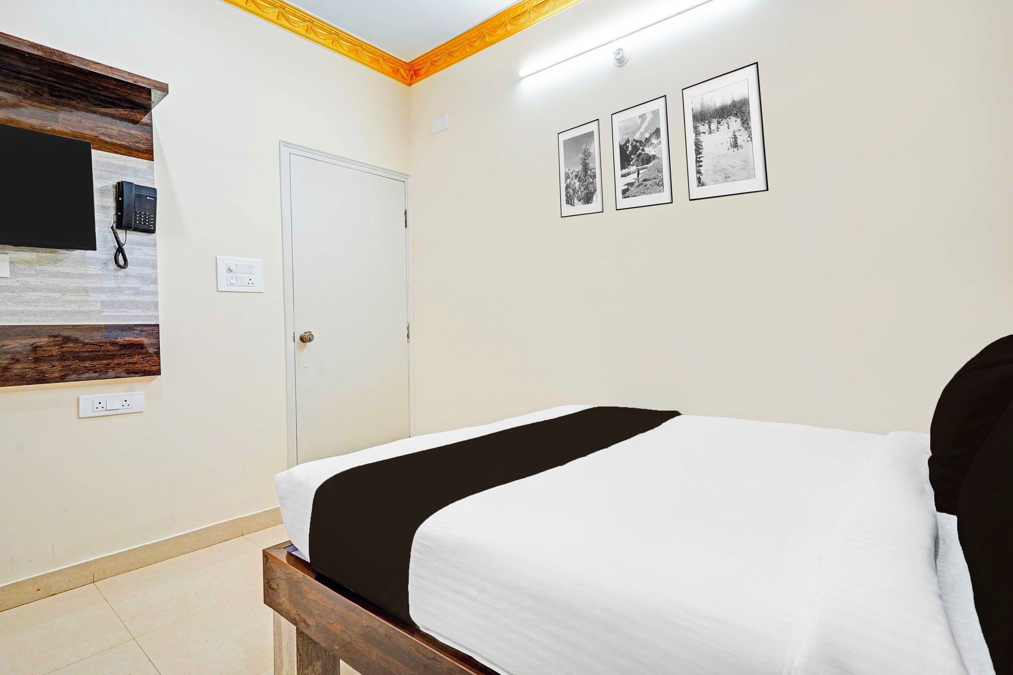A hotel room with a bed, a telephone, a door, and three framed pictures on the wall.