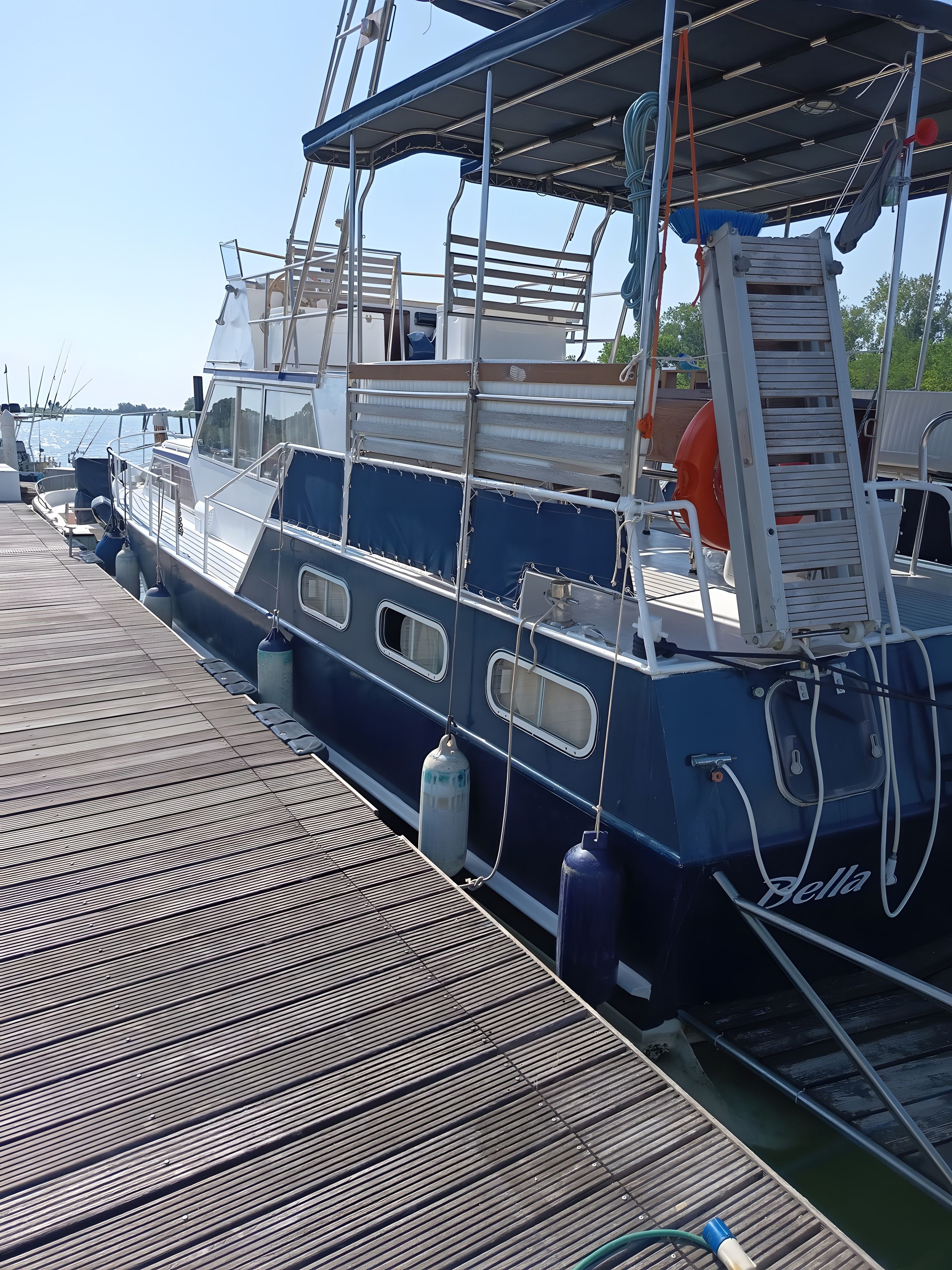 A boat docked at a pier with a wooden deck, metal railings, and a ladder.