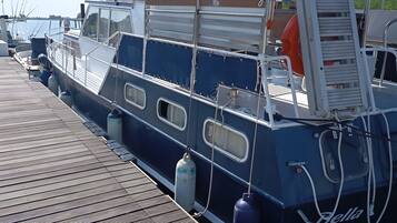 A boat docked at a pier with a wooden deck, metal railings, and a ladder.