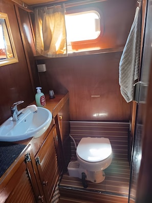 Ein kleines Badezimmer mit einem weißen Waschbecken, einer Toilette und einem Fenster mit Vorhängen.