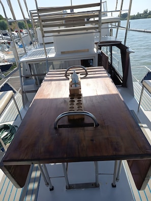 Ein Bootsdeck mit Holztisch, Metallgeländern und Blick auf das Wasser.