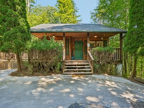 A wooden cabin with a green door, a porch, and a staircase leading to the entrance. - Bear Crest | Hot Tub, Pet-Friendly (Gatlinburg)