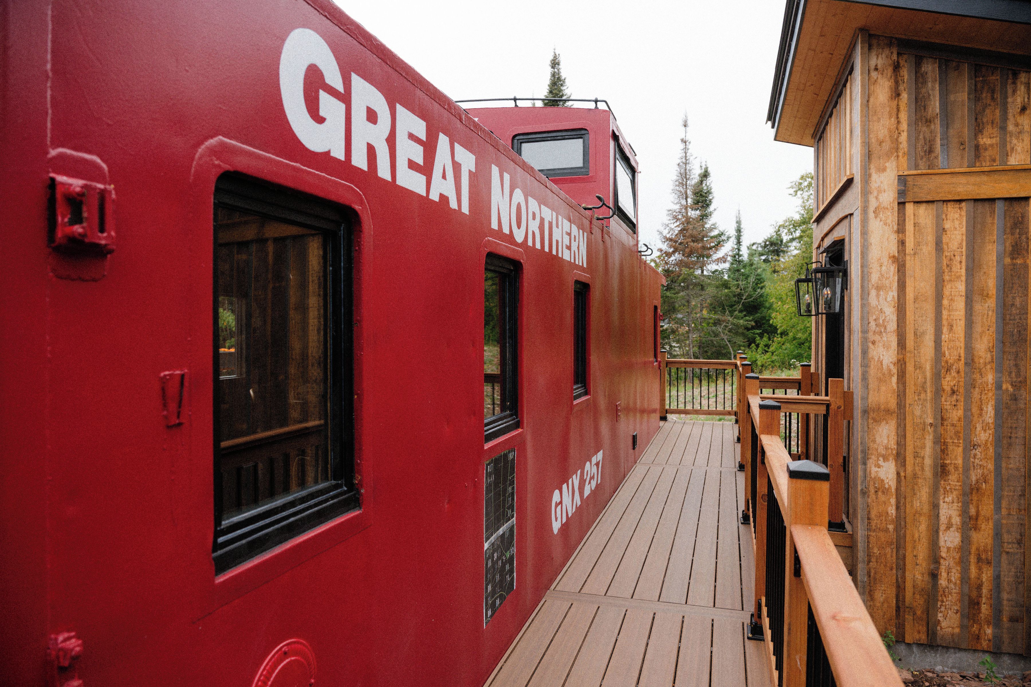 Un vagón de tren rojo con la inscripción 'GREAT NORTHERN', una cubierta de madera y vistas a árboles.