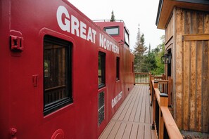 Un vagón de tren rojo con la inscripción 'GREAT NORTHERN', una cubierta de madera y vistas a árboles.