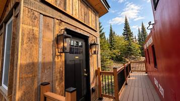 A wooden building with a black door, two wall-mounted lanterns, and a wooden deck with a railing.