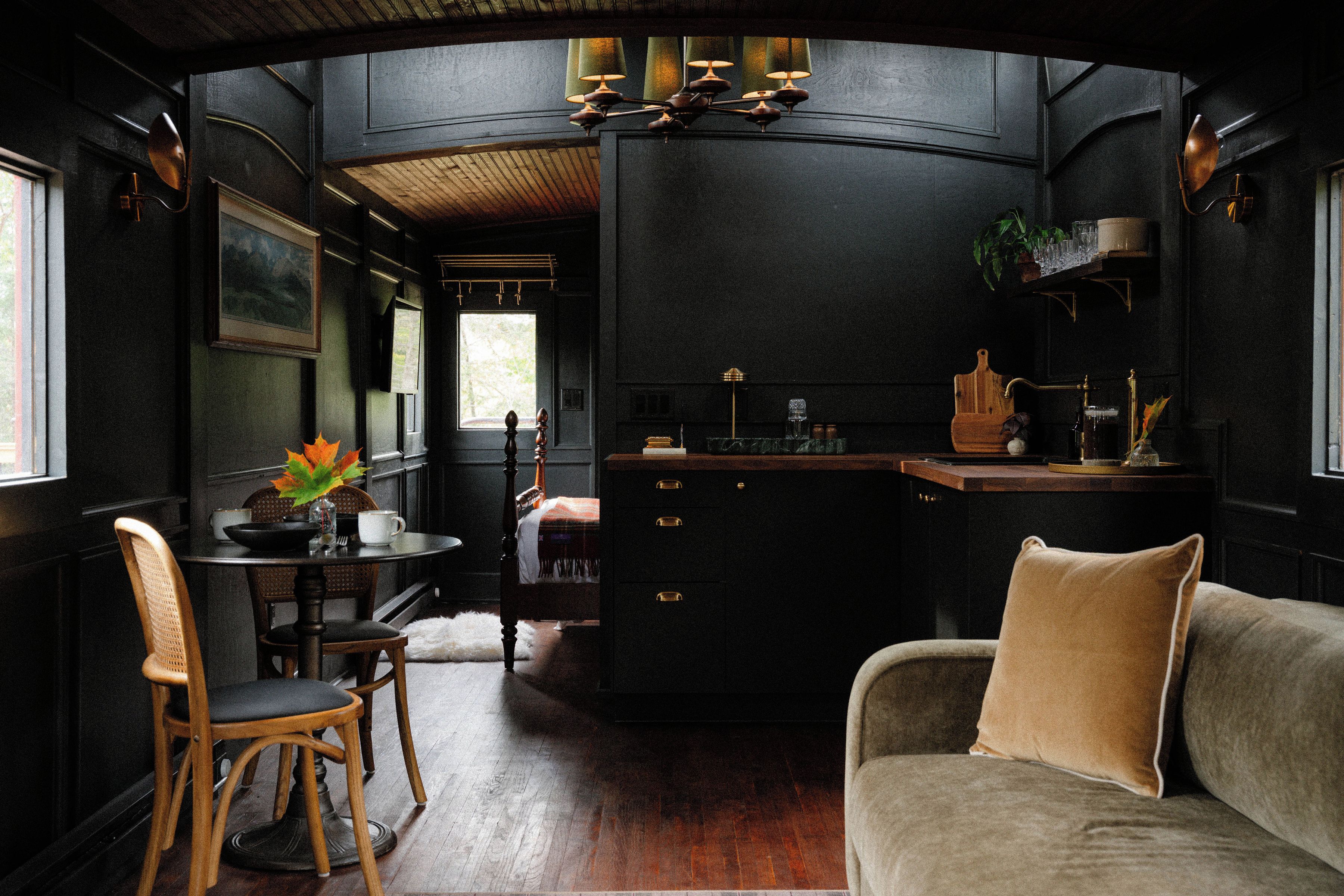 Un interior compacto, con una decoración oscura, que incluye un comedor, un sofá y una encimera de cocina.
