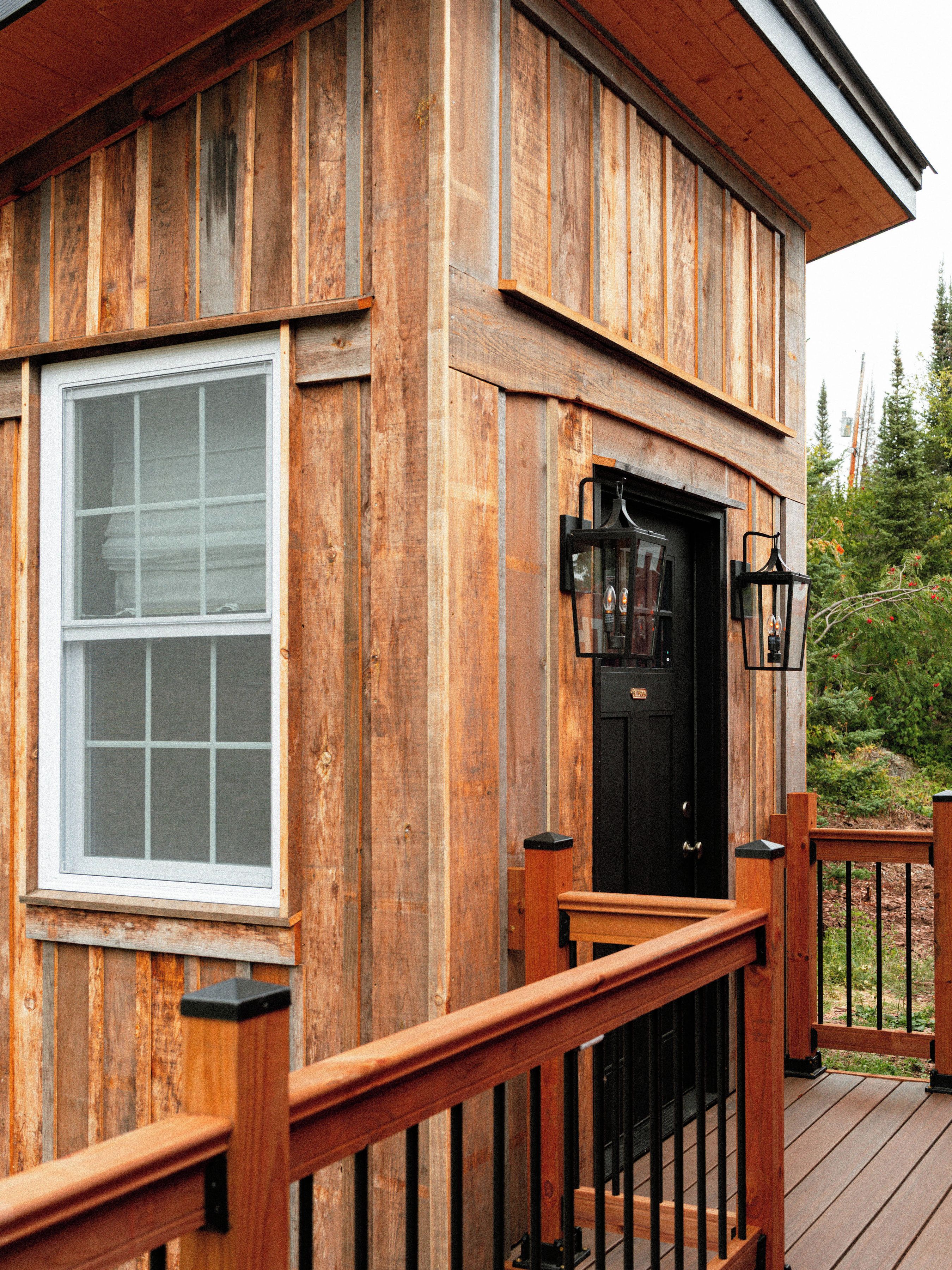 Une cabane en bois avec une porte noire, une fenêtre et une terrasse en bois.