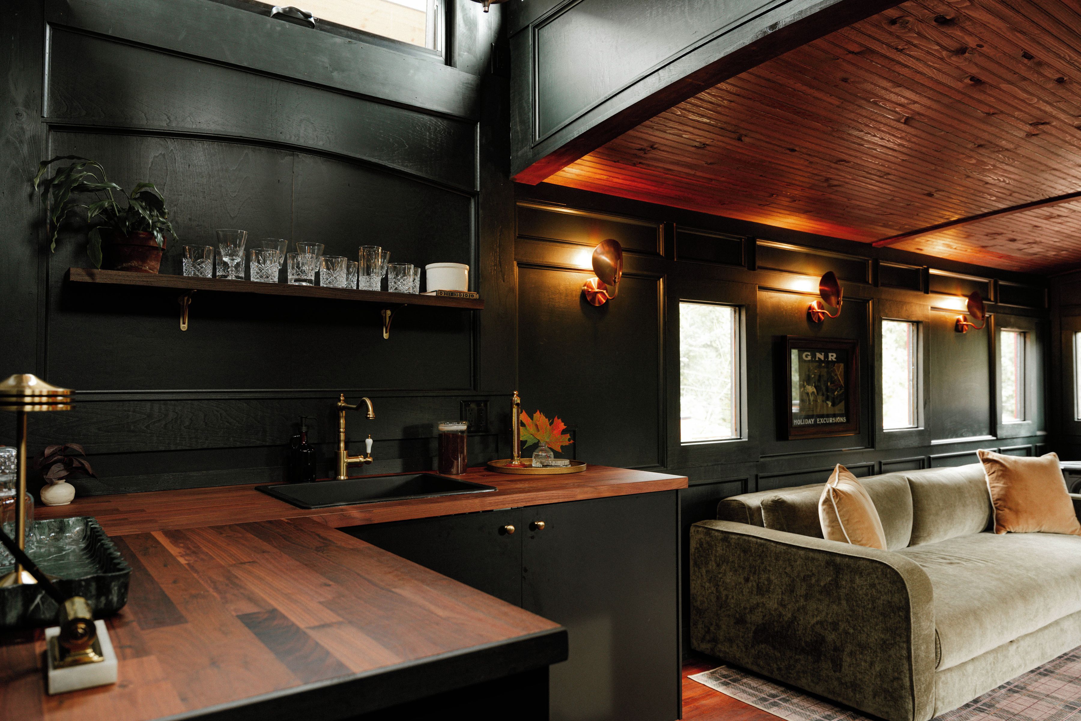 A modern kitchen with a wooden countertop and a built-in sink. There is a sofa and a window with a view of the outdoors.