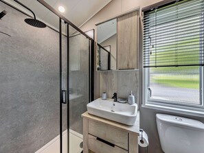A modern bathroom with a glass-enclosed shower, a sink with a mirror above, and a toilet with a window view. - Prion 1.0 Spa (Denbigh)
