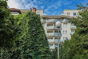 Um edifício residencial com várias andares, varandas, um poste de luz e muita vegetação.