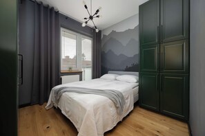 Quarto com cama, janela com persianas, luminária fixa na parede e guarda-roupa verde.