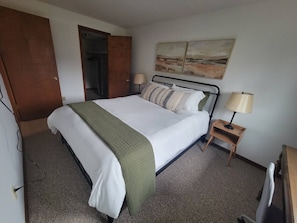 A hotel room with a bed, a nightstand with a lamp, a painting on the wall, and a wardrobe. - Century Noll | Whole Duplex, 3BR, Yard, Pets, Mayo (Rochester)