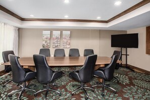 Un salón de conferencias con una larga mesa, sillas negras, un televisor de pantalla plana y una pintura de paisaje urbano en la pared.