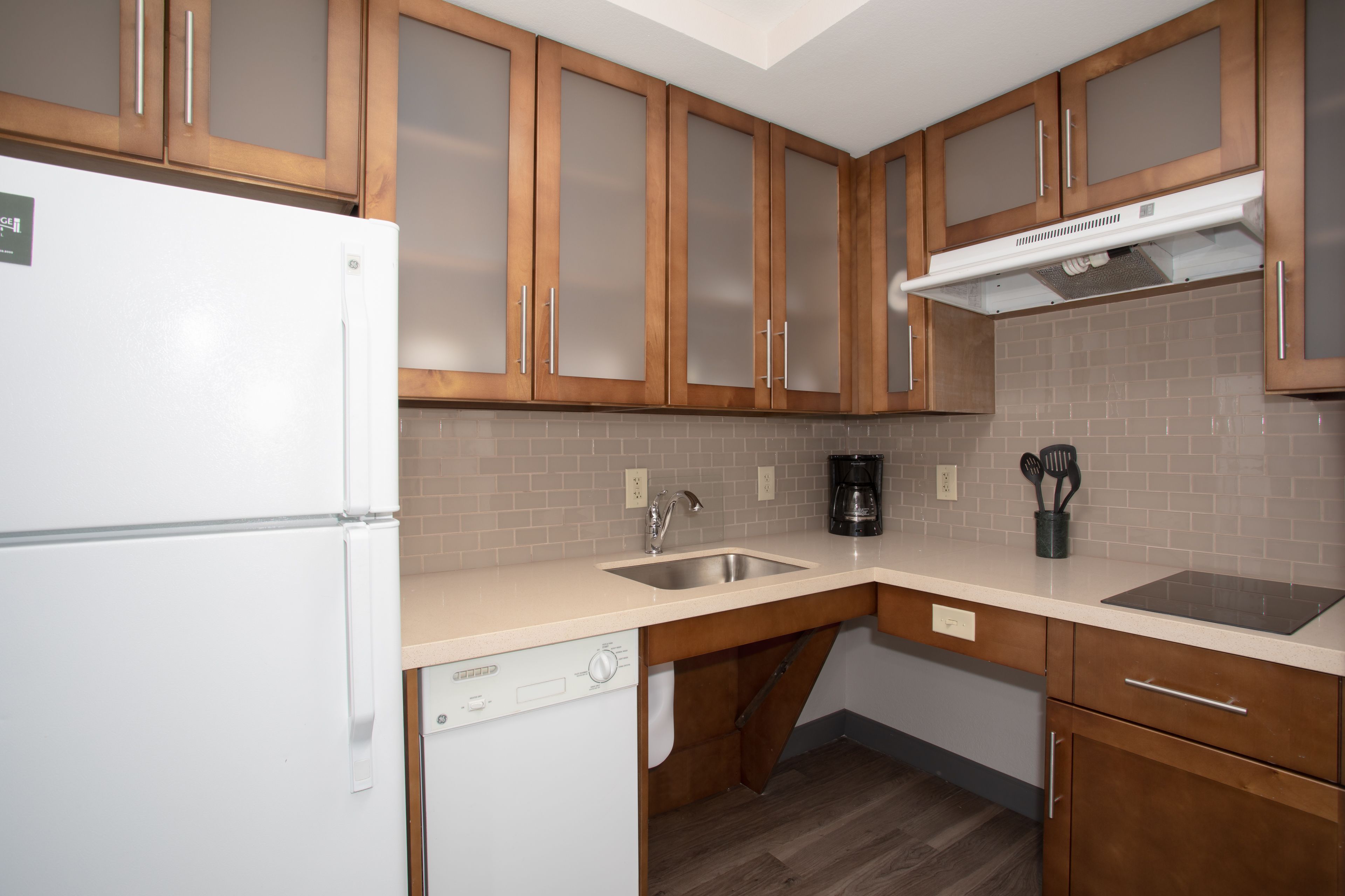 A kitchen with wooden cabinets, a white refrigerator, a dishwasher, a sink, and a coffee maker.