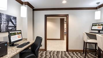 A hotel room with a desk, computer, and chair. There is a door leading to another room.
