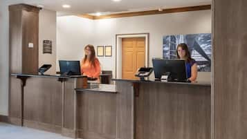 A reception area with two receptionists at desks, a wooden reception desk, a door, and framed pictures on the wall.