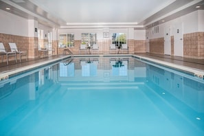 Piscina interior luminosa com borda em azulejo, trampolim e espreguiçadeiras.