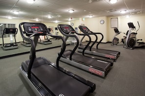 A gym with treadmills, stationary bikes, and a mirrored wall.