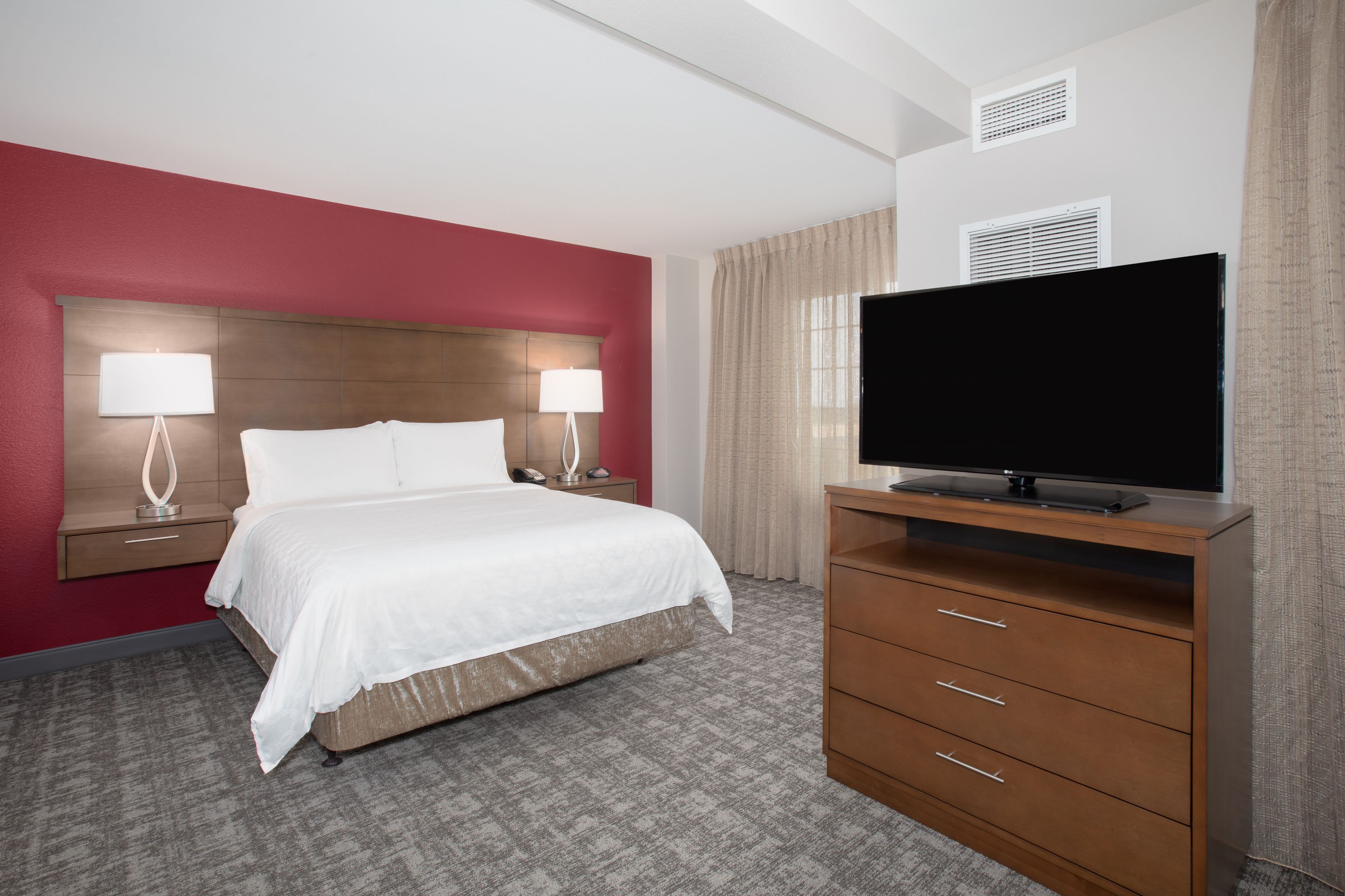 A hotel room with a bed, two bedside lamps, a TV on a wooden stand, and a carpeted floor.