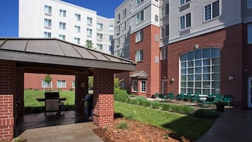 A covered outdoor area with a grill, brick building, and green chairs.
