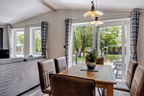 A dining area with a wooden table and leather chairs, a sofa, and a large window with curtains. - Elwy 3.0 Spa (Denbigh)