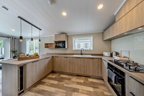 A modern kitchen with wooden cabinets, a central island, a microwave, a toaster, and a gas stove. - Elwy 3.0 Spa (Denbigh)