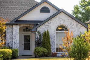 A residential building with a gabled roof, a front entrance with a door and a window, and a small porch area. - The Landing | Bike to Downtown + Coler (Bentonville)