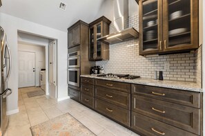 A modern kitchen with dark wood cabinets, a stainless steel range, and a tiled backsplash. - The Landing | Bike to Downtown + Coler (Bentonville)