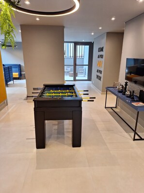 A modern indoor space with a foosball table, a seating area with a blue sofa, and a wall with motivational text. - Modern studio apartment 200m from Paulista Avenue with a closed bedroom. (SÃO PAULO)