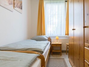 A bedroom with two beds, a window with curtains, a bedside table with a lamp, and a wardrobe. - 1 in the House Sturmmowe (St. Peter-Ording)